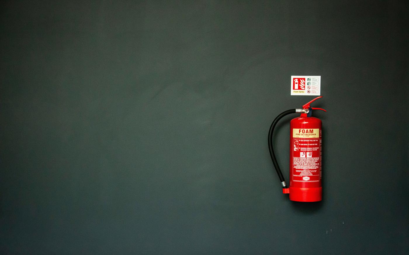 red fire extinguisher on gray wall by Tak Kei Wong courtesy of Unsplash.
