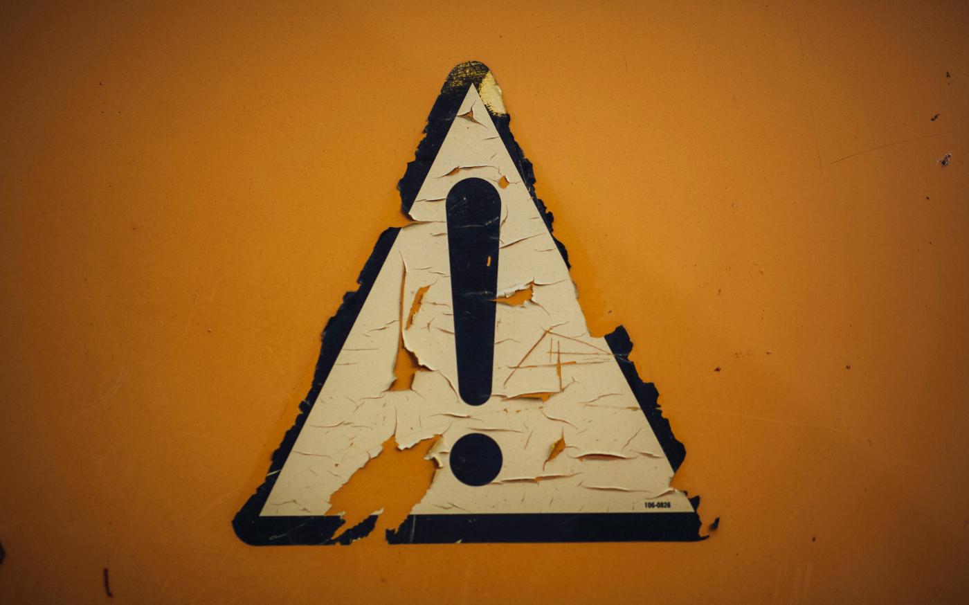 a triangle shaped sign on a yellow wall by Markus Spiske courtesy of Unsplash.