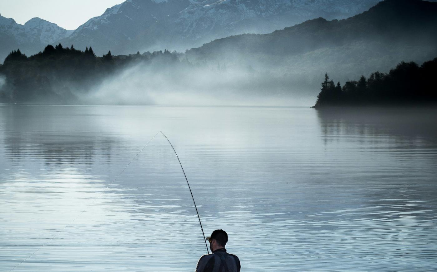 a man standing in a body of water holding a fishing pole by Domie Sharpin courtesy of Unsplash.