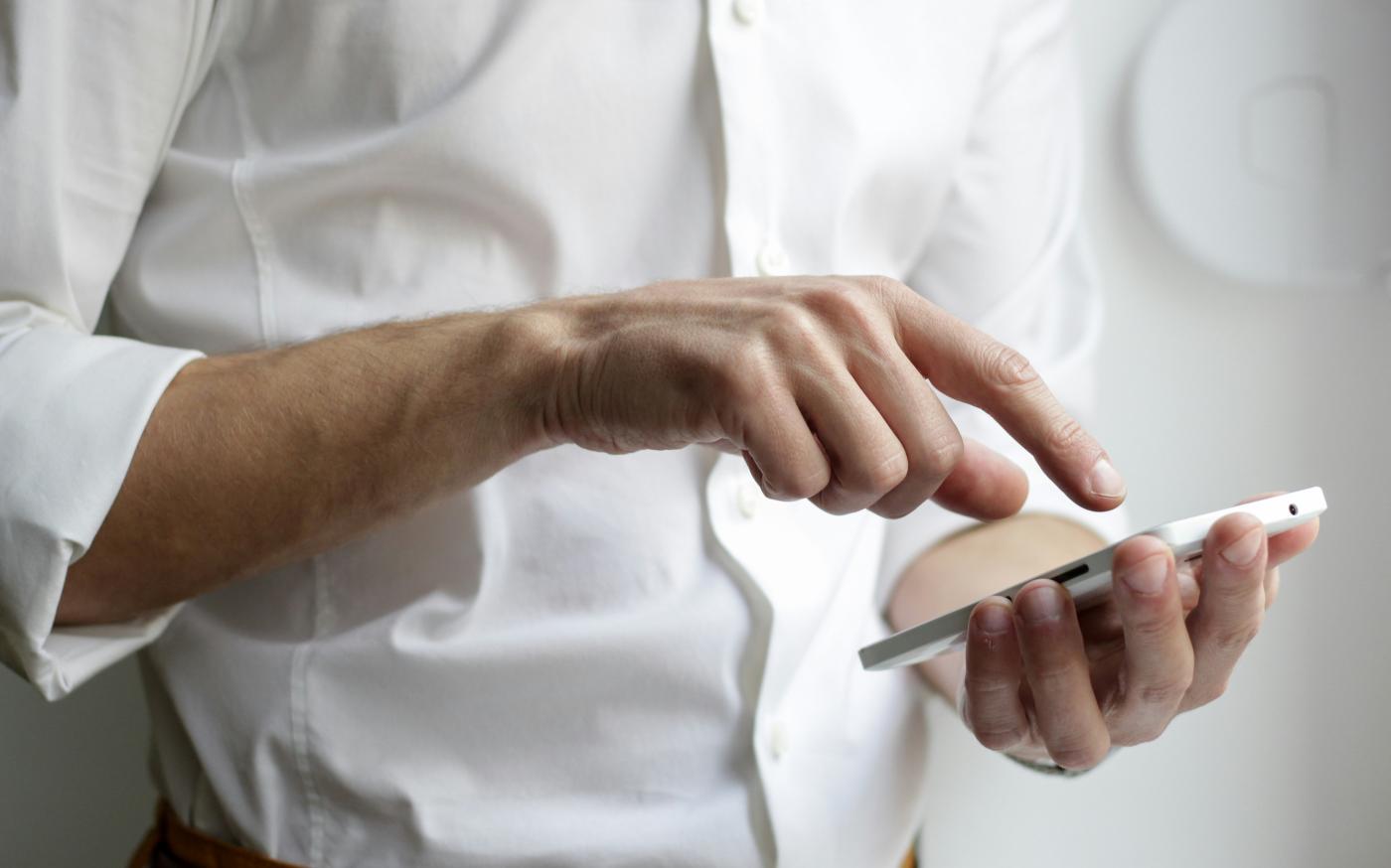 person holding white Android smartphone in white shirt by NordWood Themes courtesy of Unsplash.