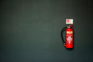 red fire extinguisher on gray wall by Tak Kei Wong courtesy of Unsplash.