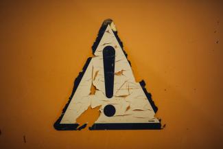 a triangle shaped sign on a yellow wall by Markus Spiske courtesy of Unsplash.