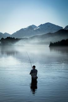 a man standing in a body of water holding a fishing pole by Domie Sharpin courtesy of Unsplash.