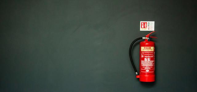 red fire extinguisher on gray wall by Tak Kei Wong courtesy of Unsplash.