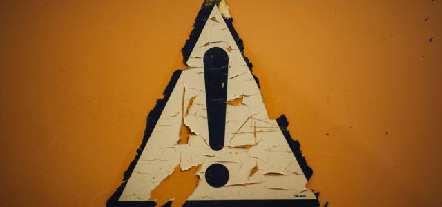 a triangle shaped sign on a yellow wall by Markus Spiske courtesy of Unsplash.