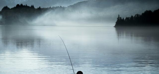 a man standing in a body of water holding a fishing pole by Domie Sharpin courtesy of Unsplash.